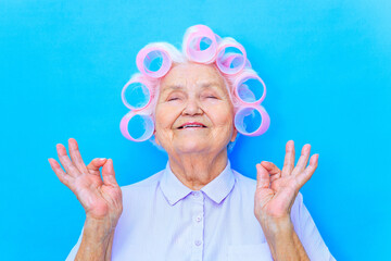 cute 80 years old woman with curlers on white hair looking happy in blue studio background