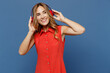© ViDi Studio - Young smiling fun happy minded caucasian woman 30s she wear red dress headphones listen music look aside on workspace isolated on plain dark royal navy blue background studio People lifestyle concept.