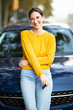 Happy young woman in front of her new car outside