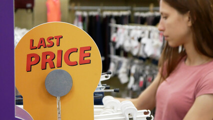 Wall Mural - A sign LAST PRICE in a clothing store and a woman choosing the clothes behind it