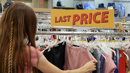 Wall Mural - A big sign LAST PRICE in a clothing store and a woman choosing the clothes
