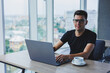 © Дмитрий Ткачук - Cheerful businessman in glasses sits at his desk, working with a laptop in the office. A businessman sits and works on a laptop computer and drinks coffee. Starting the day at the office