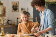 © Mediaphotos - Young woman preparing vegetable salad with her little son helping her at table in kitchen