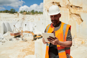 Aufkleber - Middle aged foreman with tablet looking through online instruction at workplace while standing against wall built up of marble blocks