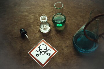 Glass flasks with a dangerous toxic substance on an old table. An emblem with a skull in a red square. Production of harmful substances.