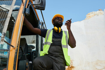 Aufkleber - Young serious African American worker or foreman with walkie-talkie holding by door of construction machine while standing in its cab