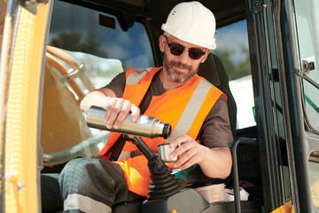 Aufkleber - Male driver of construction machine pouring hot tea or water from thermos over gearshift while sitting in front of steer