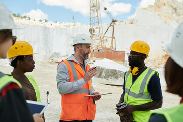 Aufkleber - Confident middle aged foreman with document giving working instructions to African American subordinates at meeting