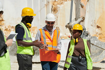 Aufkleber - Group of interracial workers in hardhats and uniform discussing working plan at meeting while confident foreman pointing at document