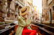 Rear, back view of elegant woman wearing straw hat on Gondola ride along beautiful street in Venice, Italy. Travel, vacation, lifestyle conception. Copy, empty space for text