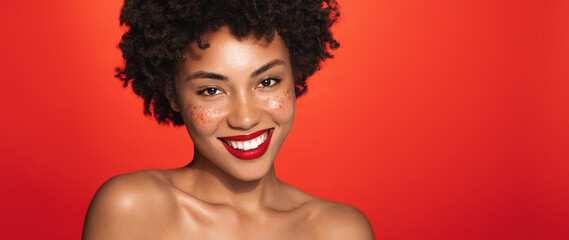 Wall Mural - Spa and cosmetology. Smiling beauty african american woman, curly hair and red lipstick, looking happy at camera, has natural hydrated facial skin, red background