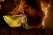 mujer joven posando con alas de isis de color amarillo, semidesnuda con fondo de fuego