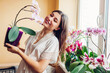 Portrait of woman admiring blooming phalaenopsis orchid holding pot. Gardener takes care of home plants and flowers.