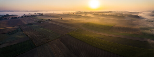 Vibrant yellow rising sun over green brown and gold farm fields with foggy background. Farm landscape of Roztocze Poland. Birseye view horizontal shot. High quality photo