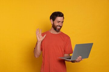 Handsome man with laptop on orange background