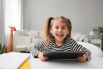 Canvas Print - Adorable little girl doing homework with tablet and earphones at table indoors