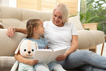 Wall Mural - Happy grandmother with her granddaughter reading book together at home