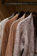 © TatjanaMeininger - close up of pastel warm knitted cardigan sweater hanging in the closet. Cozy fall and winter wardrobe.