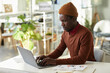 © Seventyfour - Side view portrait of young black man working with laptop at office workplace and analyzing marketing data, copy space