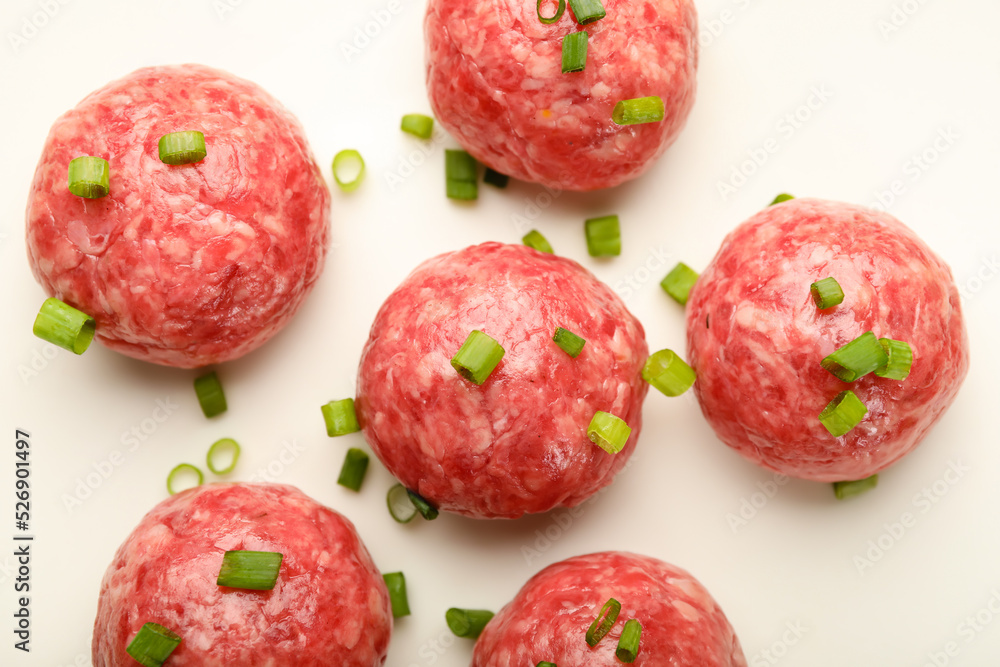 Raw meat balls with cut green onion on white plate, closeup
