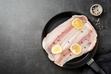 Wall Mural - Raw pangasius fish fillet with lemon and spice in frying pan on concrete background