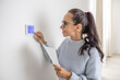 Smiling woman operates digital thermostat installed on the wall inside her home