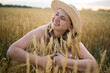 © olga_sova - A beautiful middle-aged farmer woman in a straw hat and a plaid shirt stands in a field of golden ripening wheat during the daytime in the sunlight