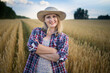 © olga_sova - A beautiful middle-aged farmer woman in a straw hat and a plaid shirt stands in a field of golden ripening wheat during the daytime in the sunlight