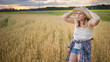 © olga_sova - A beautiful middle-aged farmer woman in a straw hat and a plaid shirt stands in a field of golden ripening wheat during the daytime in the sunlight