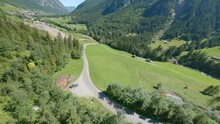 Aerial cinematography showing camper van parked on road amidst huge green mountains in Austria.