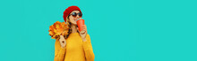 Autumn Portrait Of Happy Smiling Young Woman With Yellow Maple Leaves And Cup Of Coffee Wearing Knitted Sweater, Red Beret On Blue Background