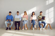 © Studio Romantic - Group of young people sitting along the wall in an office corridor, waiting for job interviews or business appointments, reading documents, going over their notes and using laptop and tablet computers