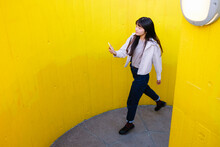 Young Woman Using Mobile Phone Walking Amidst Yellow Walls