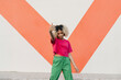 © VISTA by Westend61 - Young woman gesturing horn sign in front of wall