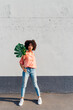 © VISTA by Westend61 - Young woman holding monstera leaf in front of wall