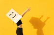 © VISTA by Westend61 - Happy woman wearing box with smiley face dancing by yellow wall