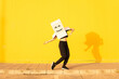 © VISTA by Westend61 - Woman wearing box with smiley face enjoying dance in front of of yellow wall on footpath