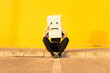 © VISTA by Westend61 - Woman wearing box with sad face sitting in front of yellow wall