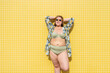 © VISTA by Westend61 - Smiling plus size woman with hands behind head in front of yellow wall