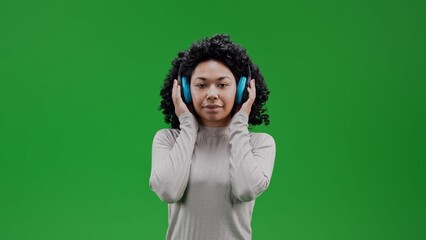 African woman with curly hair standing and holding headphones by hands in chroma key background