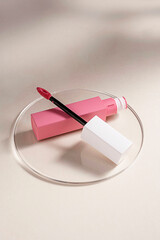 Pink liquid lipstick and applicator brush with open tube. Makeup cosmetic product. Neutral, warm background