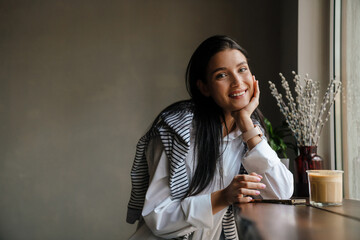 White woman smiling and using cellphone while sitting at cafe