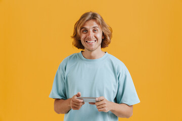 Young ginger man wearing t-shirt smiling and using mobile phone