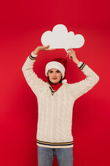 Canvas Print - smiling young woman in santa hat and sweater holding thought bubble above head isolated on red.