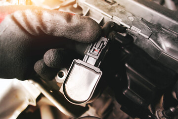 Wall Mural - The auto mechanic is unplugging the ignition coil of the car engine in the engine compartment.