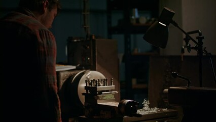 Wall Mural - Mid-adult man working indoors in metal workshop at night.