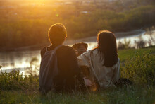 Young People In Love A Guy And A Girl Are Sitting In Nature On A High Bank Of The River With Their Pet Big Dog At Sunset Outside The City