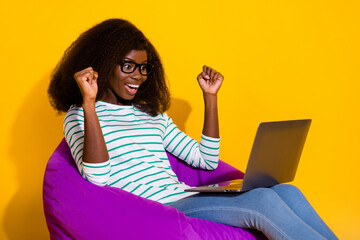 Wall Mural - Portrait of delighted funny person sit bag use netbook raise fists celebrate triumph isolated on yellow color background