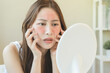 © Pormezz - Asian young woman looking face skin in the mirror have a red rash on her face from cosmetic allergy