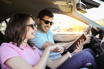 A young woman shows her boyfriend a map in a car while they’re on a trip 